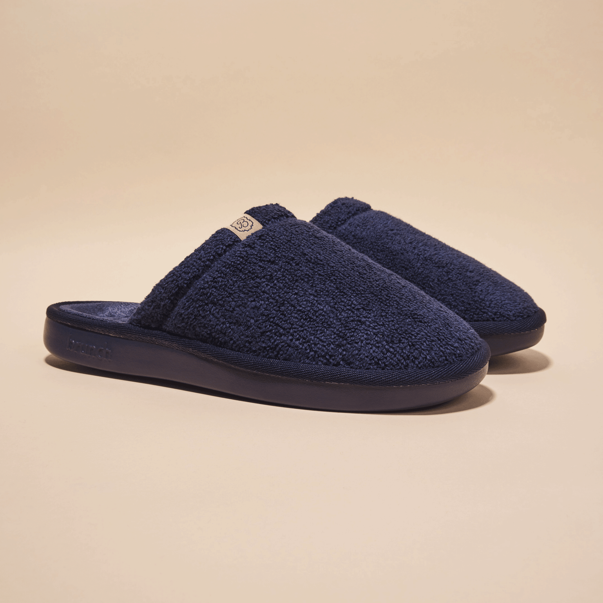 Front three-quarter view of navy Essential slipper showing plush terry upper and cushioned molded sole on beige background