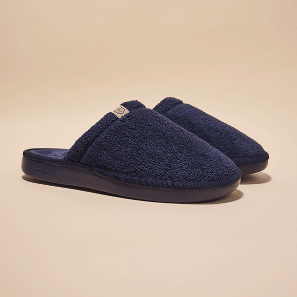 Front three-quarter view of navy Essential slipper showing plush terry upper and cushioned molded sole on beige background