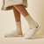 Side view of Essential Spring slipper with cream terry upper and cushioned sole worn with ribbed socks on cream background