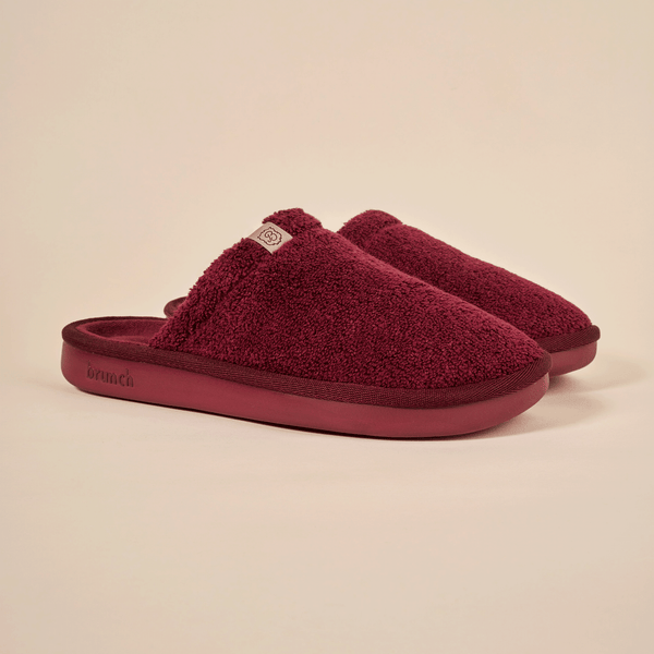 Three-quarter view of Essential slipper in burgundy showing plush terry upper and molded sole on neutral backdrop
