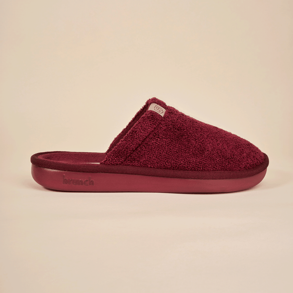 Side view of Essential slipper in burgundy with terry upper, closed-toe slip-on and embossed brunch sole on beige background