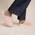 Side view of pink plush slip-on slipper showing fuzzy terry upper and molded sole on model feet with denim hem, neutral background