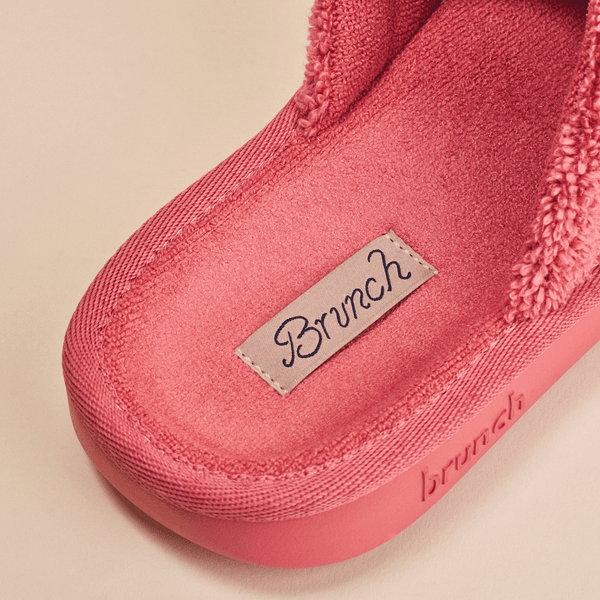 Close up of Essential slipper interior showing coral pink terry lining, stitched Brunch label and embossed Brunch logo on beige background