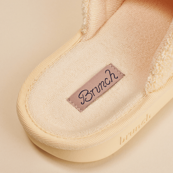Close-up of Essential slipper showing cream terry lining, stitched insole label, and embossed sole on beige background
