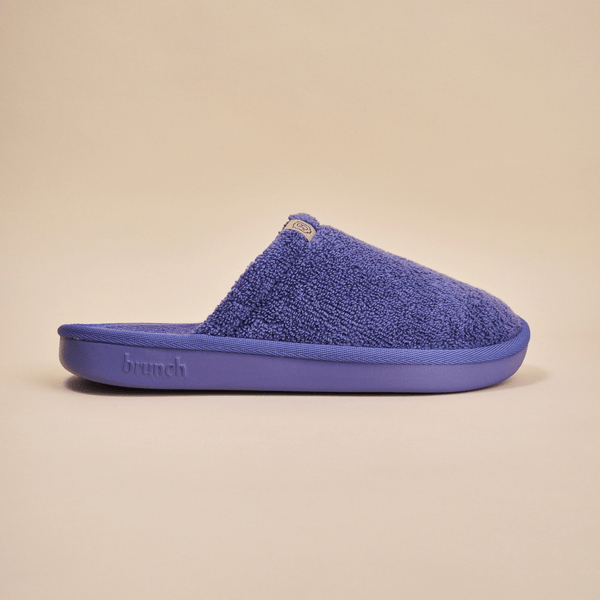 Side view of Essential slipper showing purple terry upper and molded sole embossed with brunch logo on beige background
