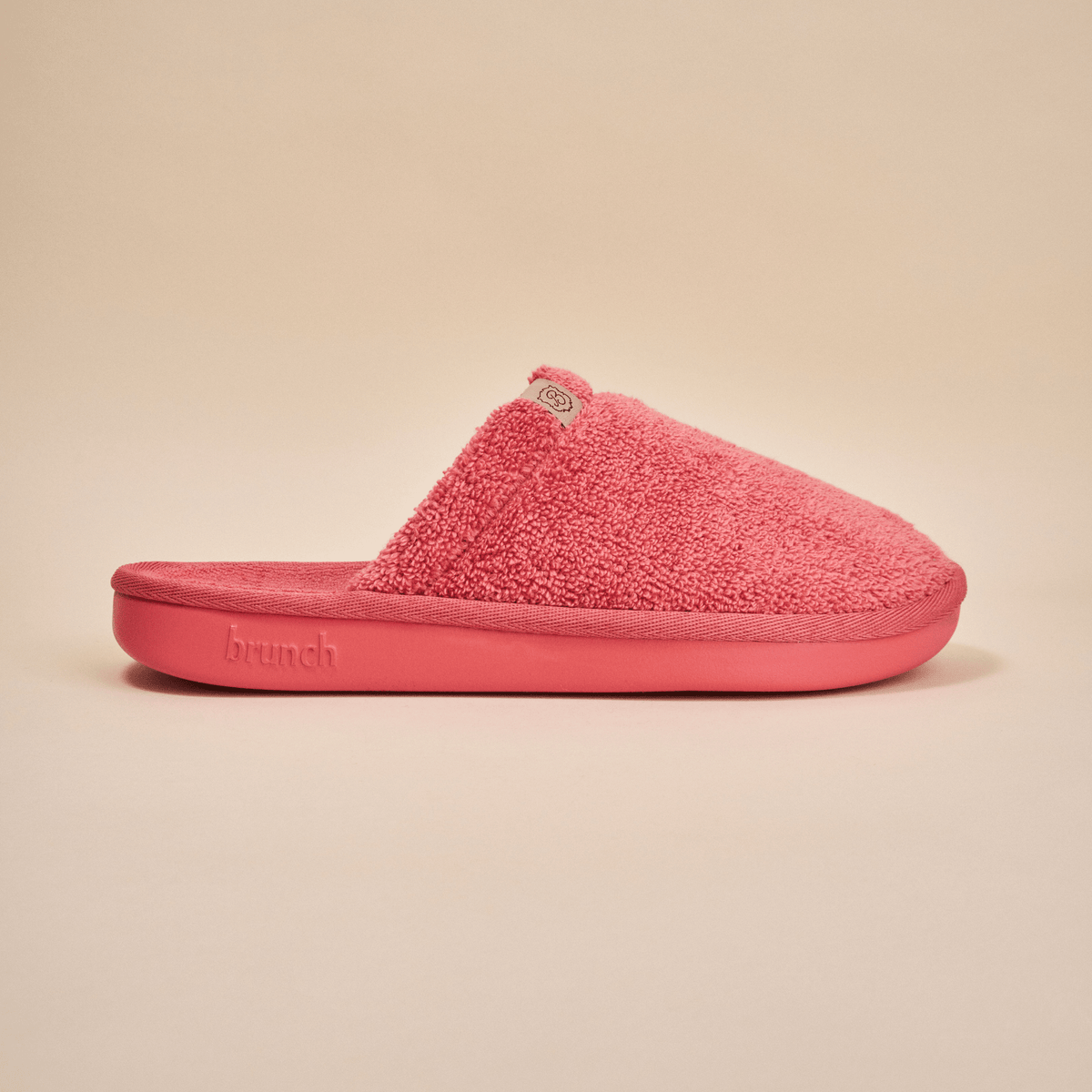Side view of Essential Slipper in coral pink showcasing terry cloth upper and molded foam sole on neutral beige background