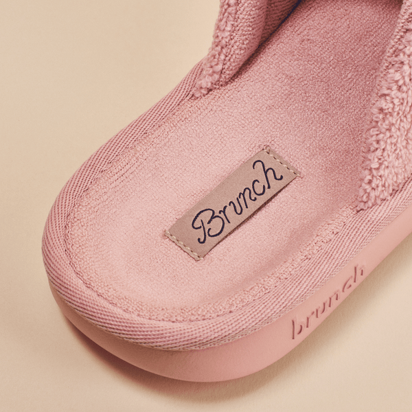 Close-up of pink Essential slipper insole showcasing plush terry lining and stitched Brunch label on beige background