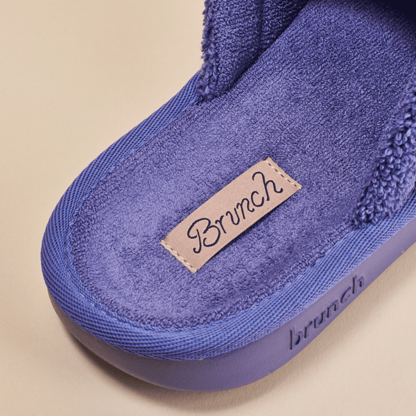 Close-up of Essential slipper interior showcasing purple terry lining, stitched ‘Brunch’ label and embossed ‘brunch’ logo on beige background