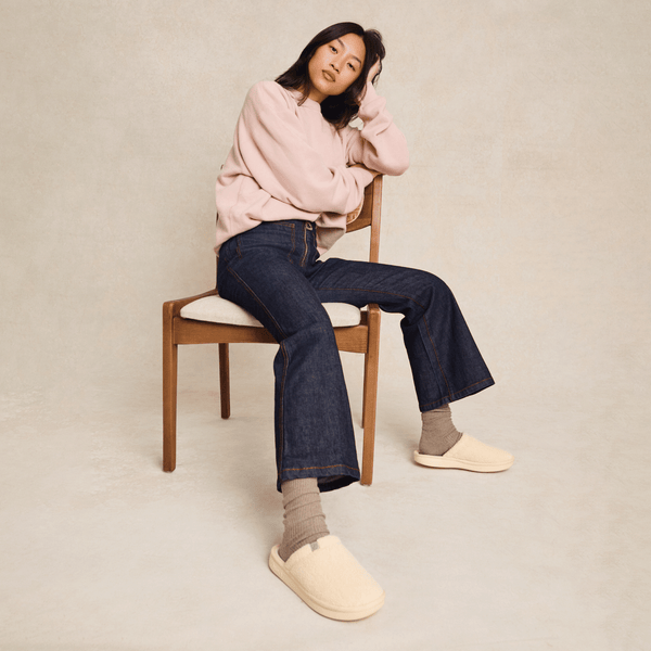 Three-quarter view of cream sherpa slipper on model showcasing slip-on design and cushioned sole against neutral studio background