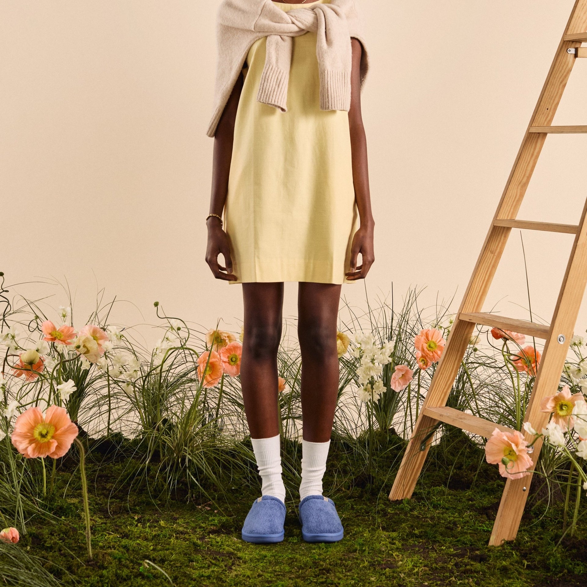 Front view of blue Essential slipper showcasing plush upper and slip-on sole on grassy floral backdrop