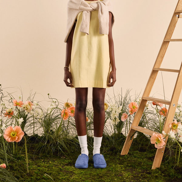 Front view of blue Essential slipper showcasing plush upper and slip-on sole on grassy floral backdrop