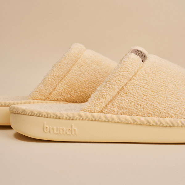 Close up view of Essential Slipper with plush terry upper and padded sole embossed with brunch logo on beige background
