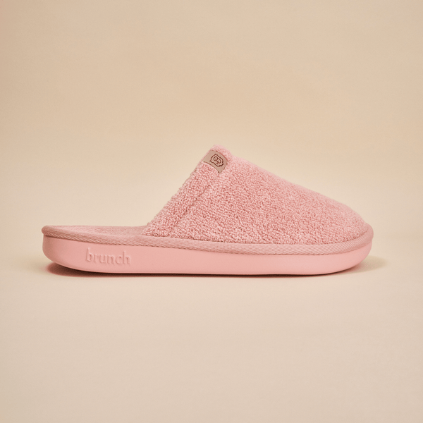 Side view of pink mule-style slipper showcasing terry cloth upper and cushioned molded sole on beige background