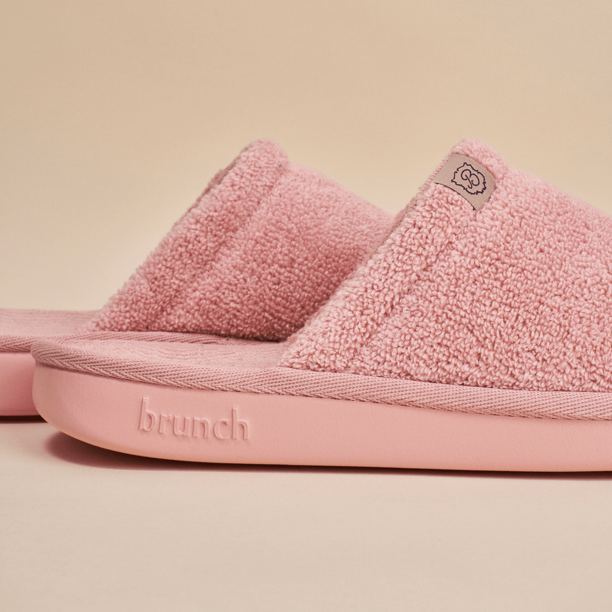 Close-up side view of pink Essential slipper showing terry-loop upper and cushioned sole with embossed brunch logo on pale beige background