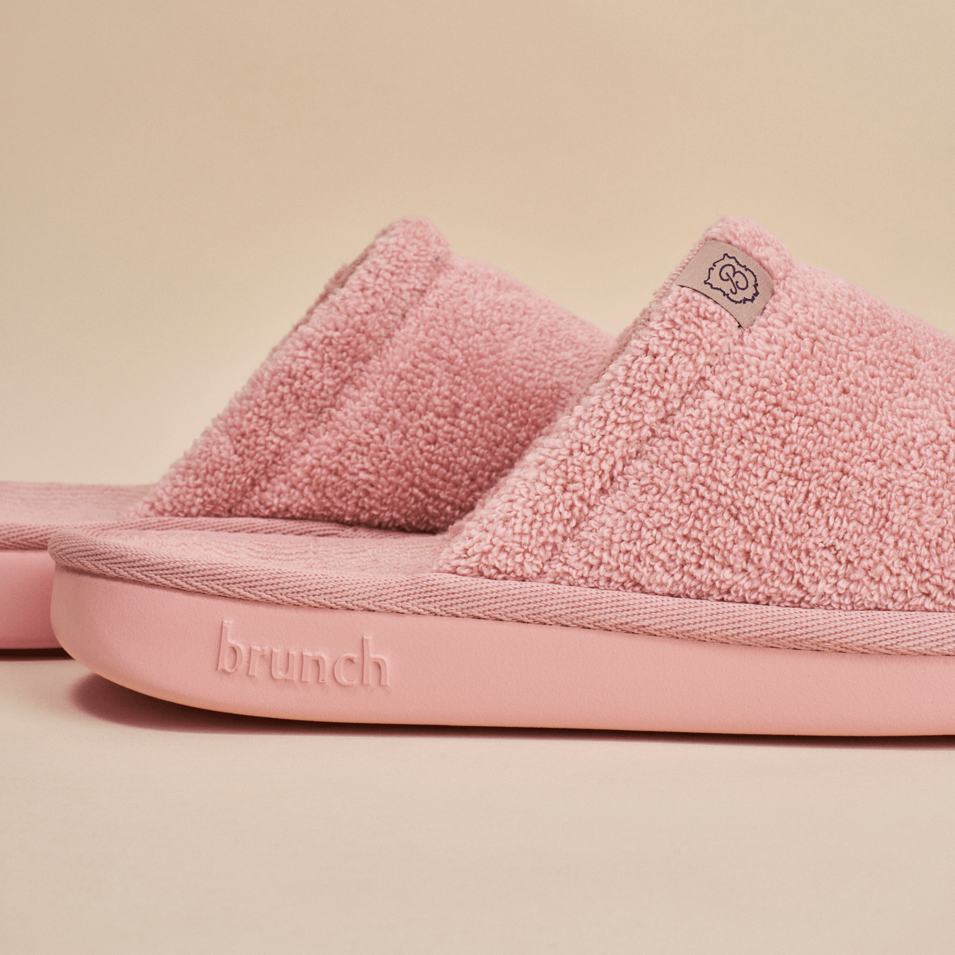 Close-up side view of pink Essential slipper showing terry-loop upper and cushioned sole with embossed brunch logo on pale beige background