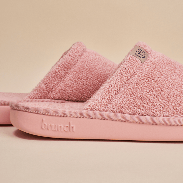 Close-up side view of pink Essential slipper showing terry-loop upper and cushioned sole with embossed brunch logo on pale beige background