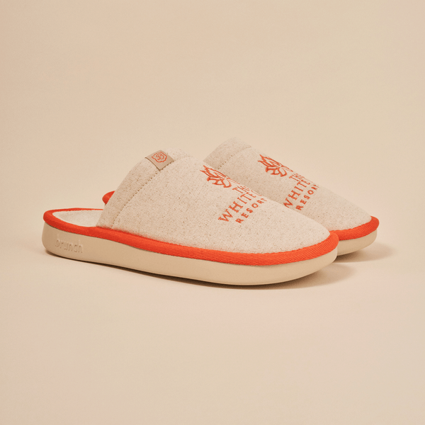 Angled view of The White Lotus slipper in beige with embroidered THE WHITE LOTUS RESORT, linen upper and orange trim