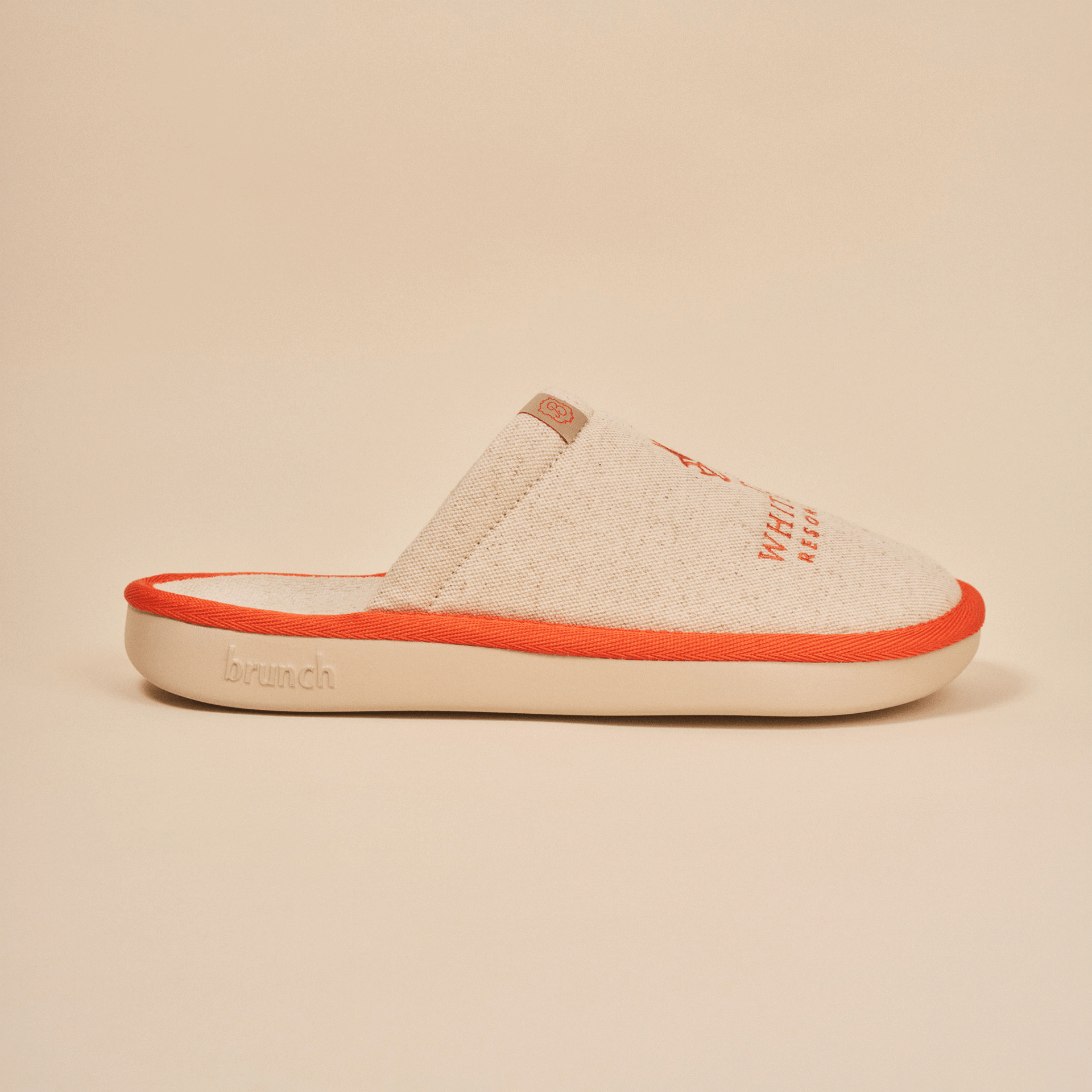 Side view of Essential The White Lotus slipper in beige showcasing linen upper, orange piping, and Brunch embossed EVA sole on neutral background