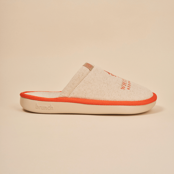 Side view of Essential The White Lotus slipper in beige showcasing linen upper, orange piping, and Brunch embossed EVA sole on neutral background