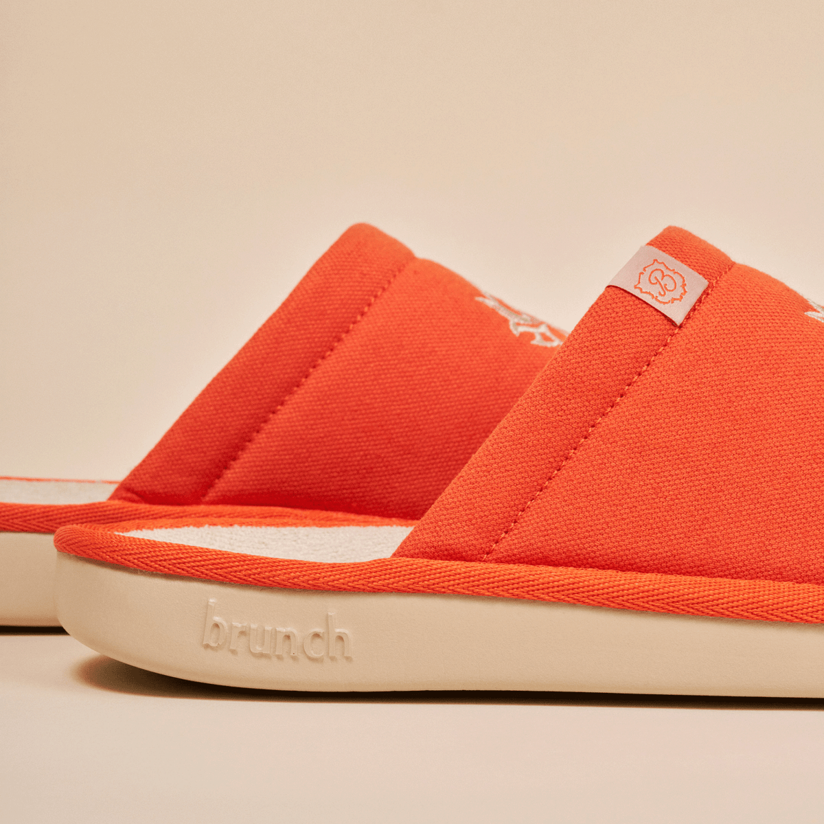 Side close up of White Lotus slipper in orange showing embroidered linen upper and embossed Brunch on cream EVA sole