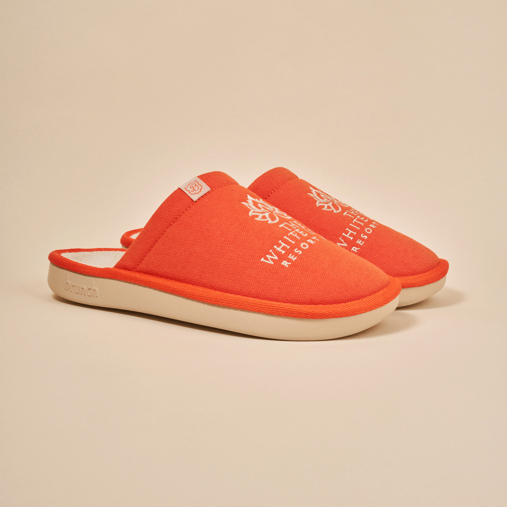 Three-quarter view of orange White Lotus slipper with embroidered White Lotus logo and EVA sole on beige background