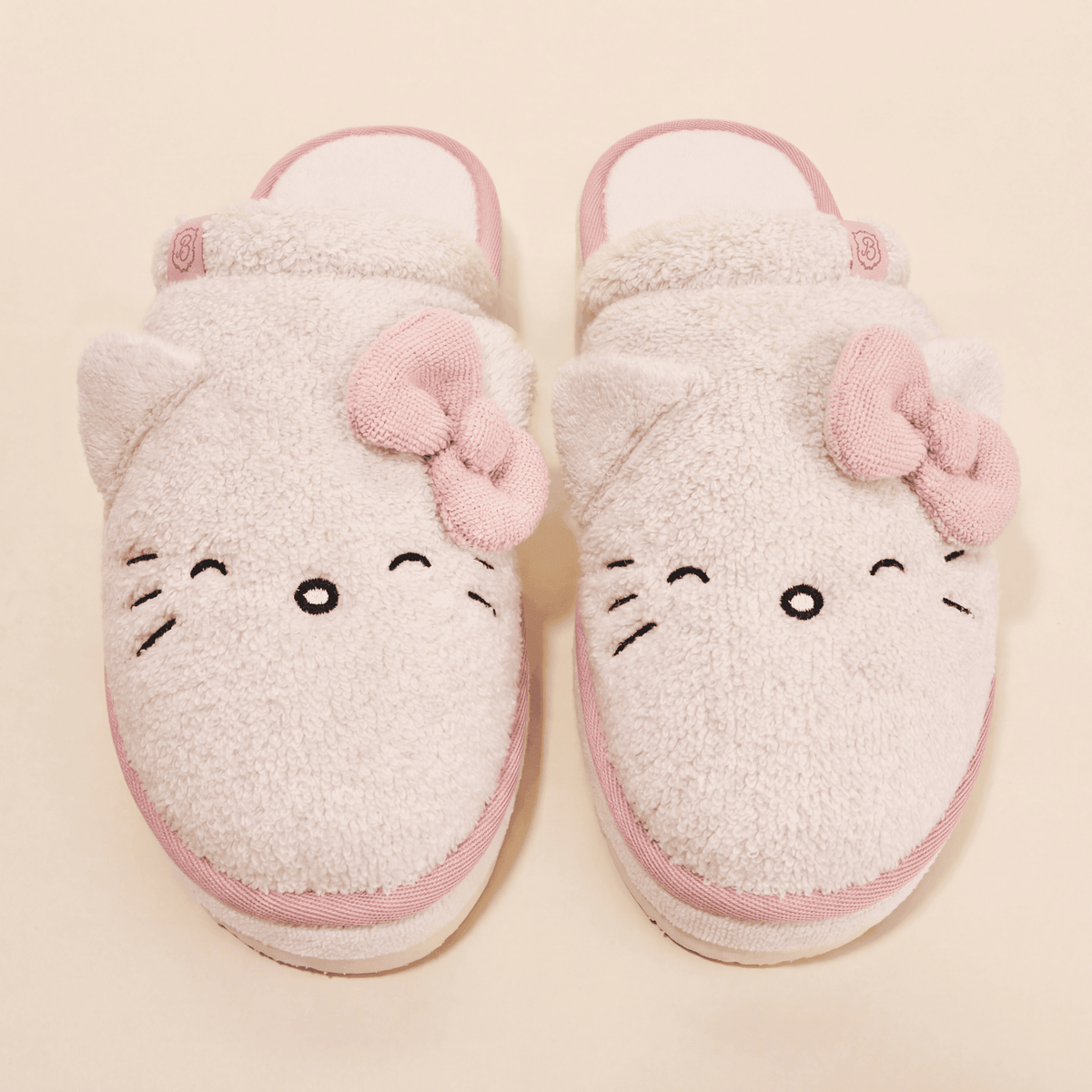 Top view of Essential XXL Hello Kitty slippers in cream terry showcasing 3D ears, pink knit bows, and embroidered whiskers on a cream background