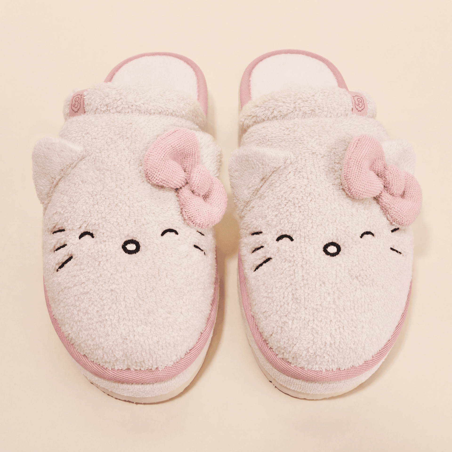 Top view of Essential XXL Hello Kitty slippers in cream terry showcasing 3D ears, pink knit bows, and embroidered whiskers on a cream background