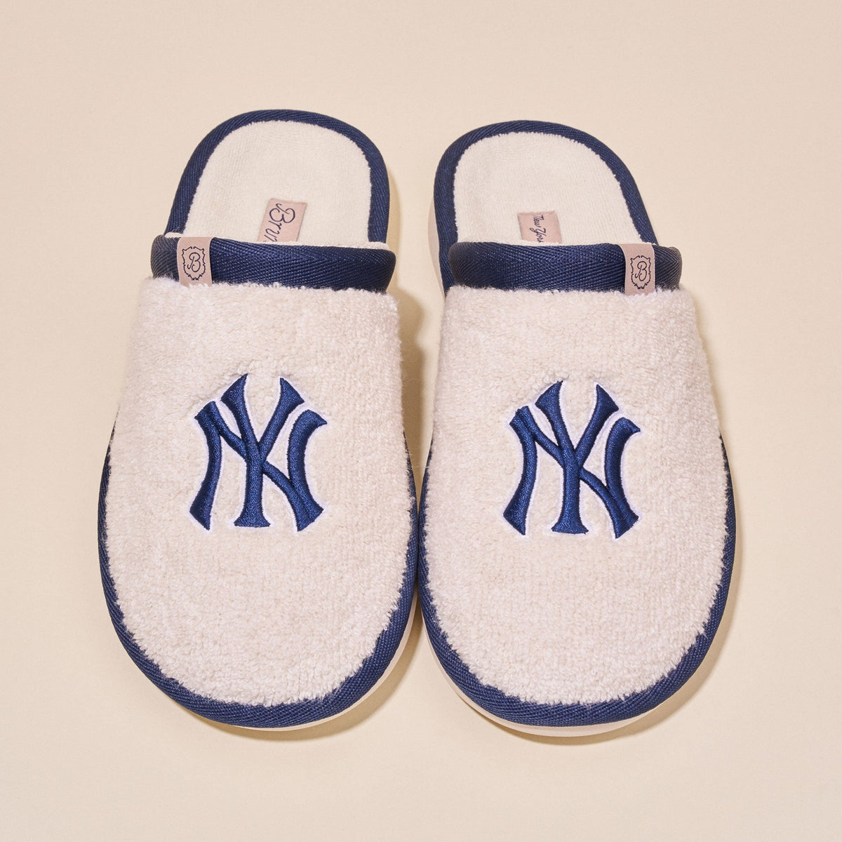 Top view of a pair of cream terry slip-on slippers showcasing embroidered navy Yankees NY logo and navy trim on a light background