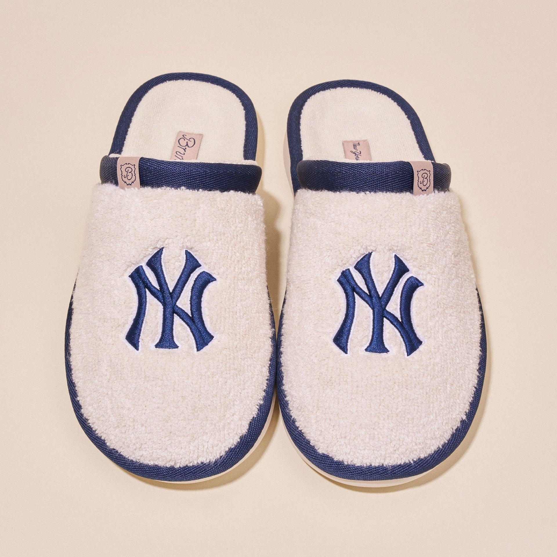 Top view of a pair of cream terry slip-on slippers showcasing embroidered navy Yankees NY logo and navy trim on a light background