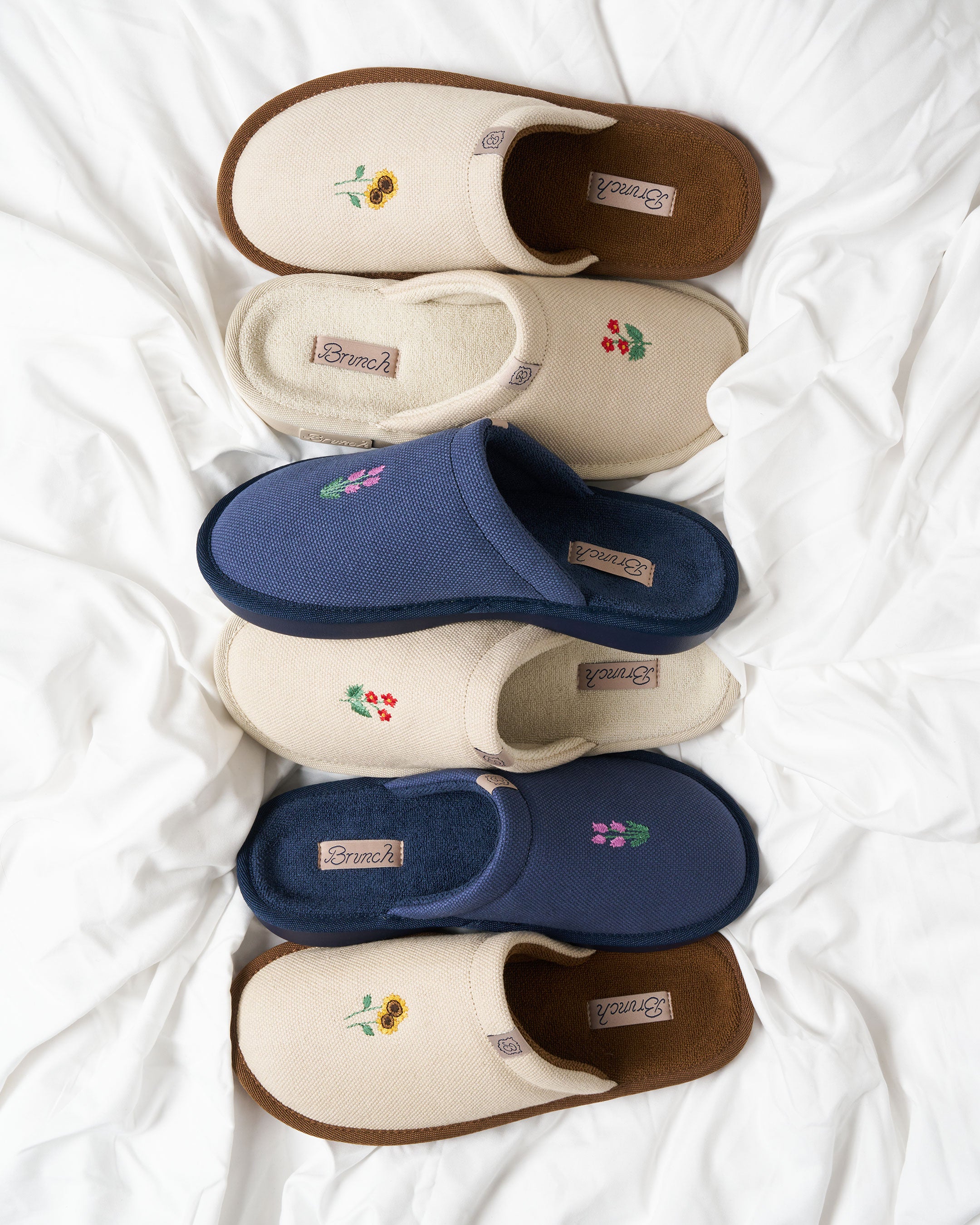 Top-down view of Essential Floral slippers showcasing embroidered floral detail on canvas uppers, multiple color pairs on a white sheet
