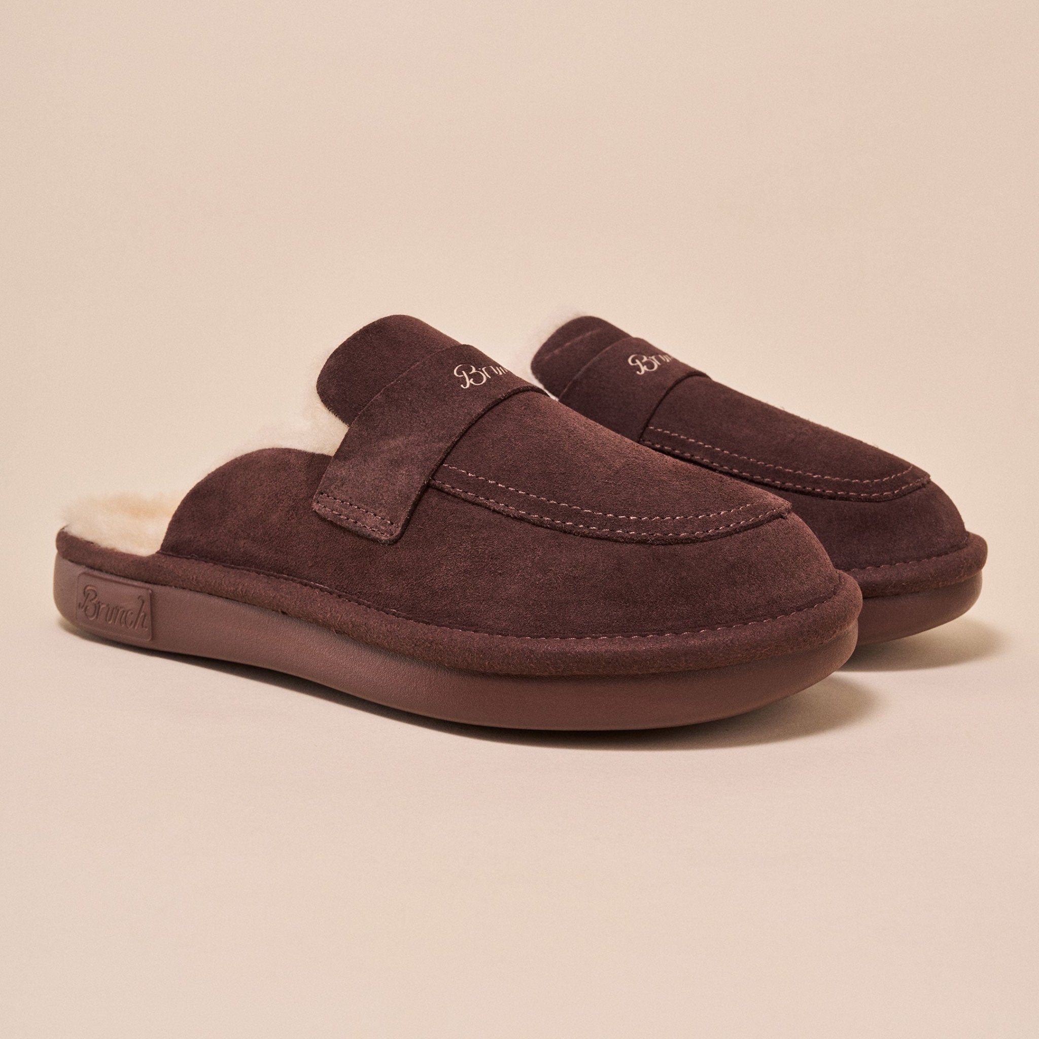 Three-quarter view of Loafer Shearling espresso brown suede slipper showcasing plush shearling lining and stitched moc toe on beige background