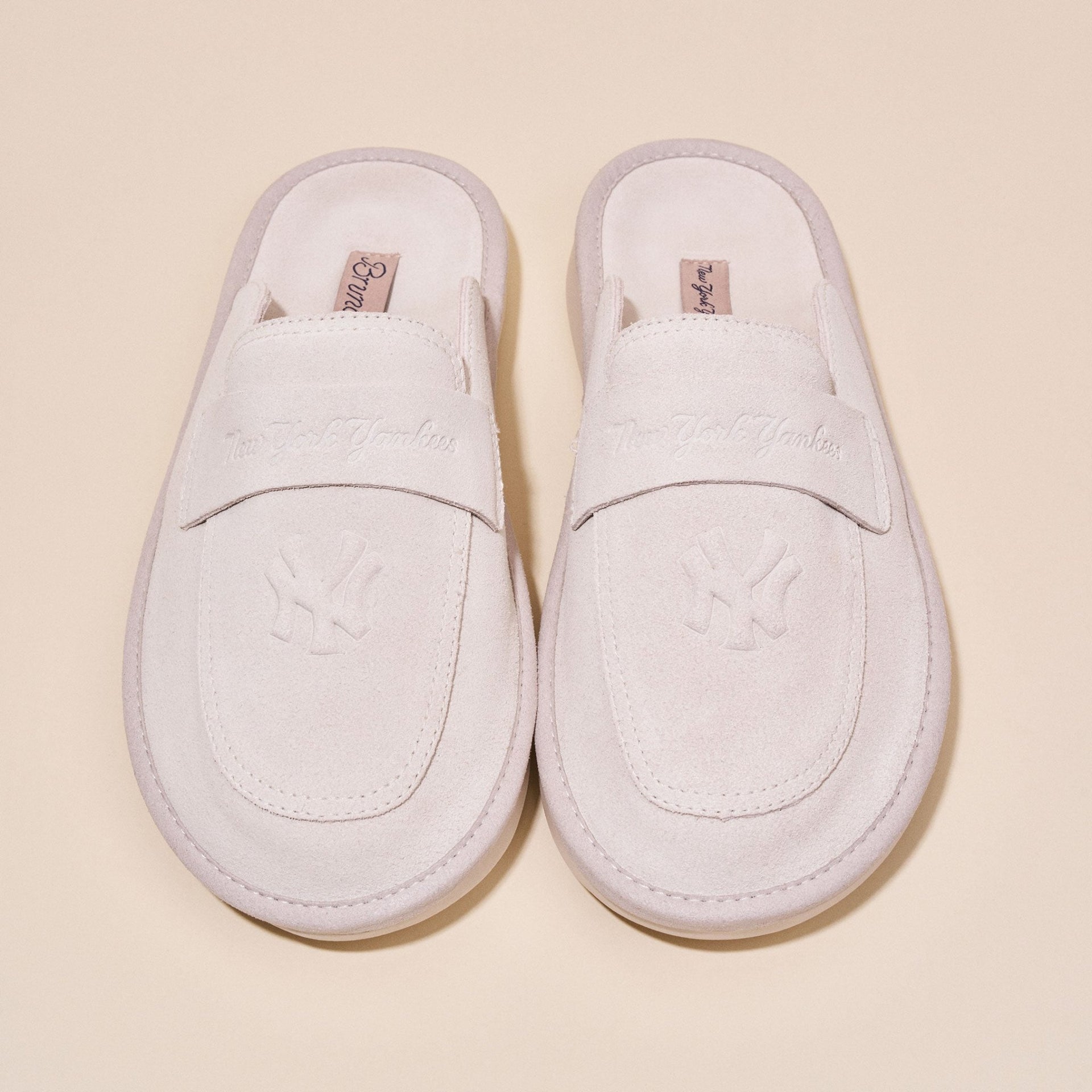 Top-down view of cream suede Yankees loafer showing embossed NY crest on vamp and penny strap on pale beige background