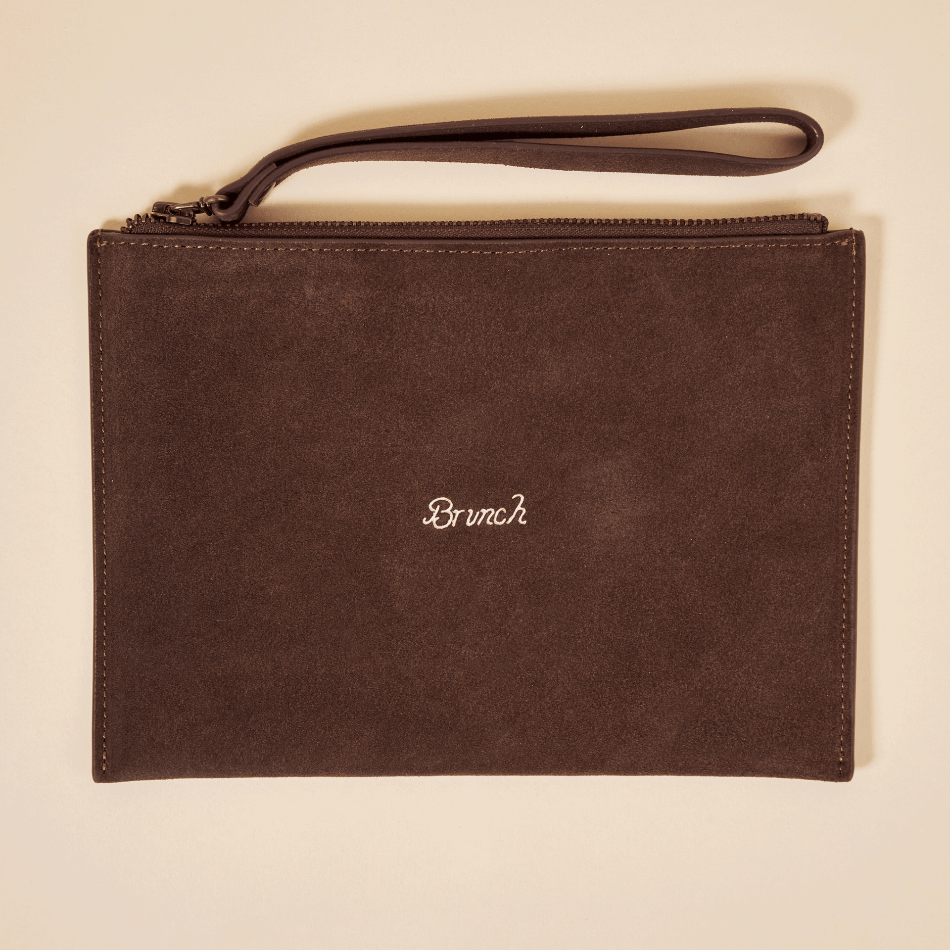 Top view of Brunch suede pouch in espresso brown showcasing embroidered Brunch logo, zip closure and wrist strap on a light beige background