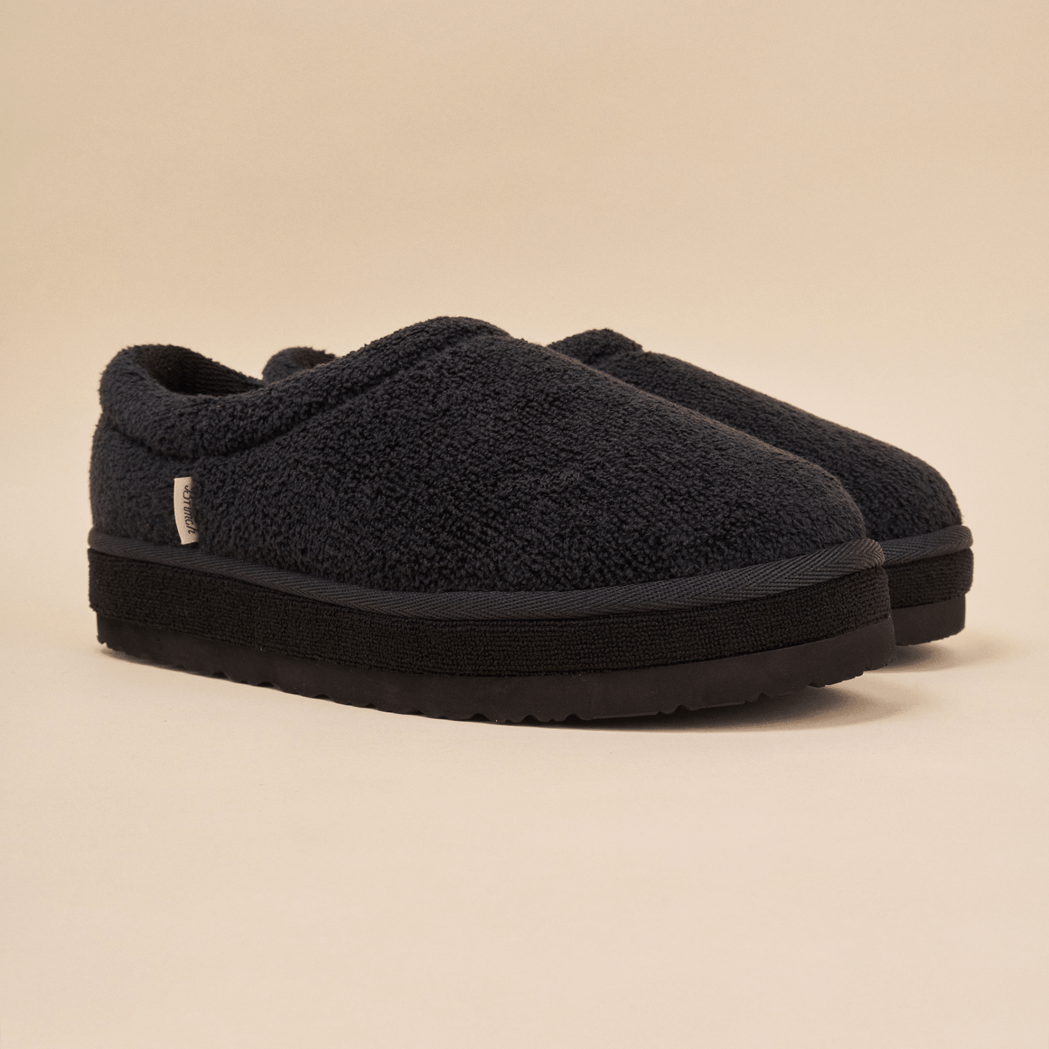 Front three-quarter view of Puff XXL slipper in black terry showcasing extra-thick platform outsole and textured terry upper on beige studio background
