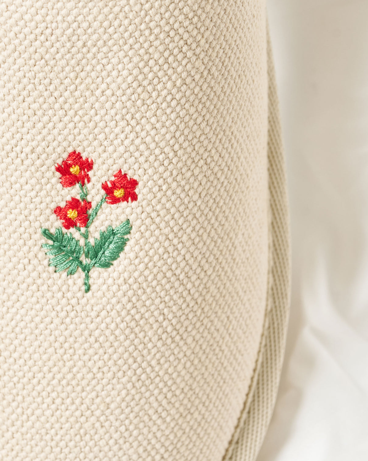 Close-up of Essential Floral canvas upper showing hand-stitched red floral embroidery on beige textured fabric