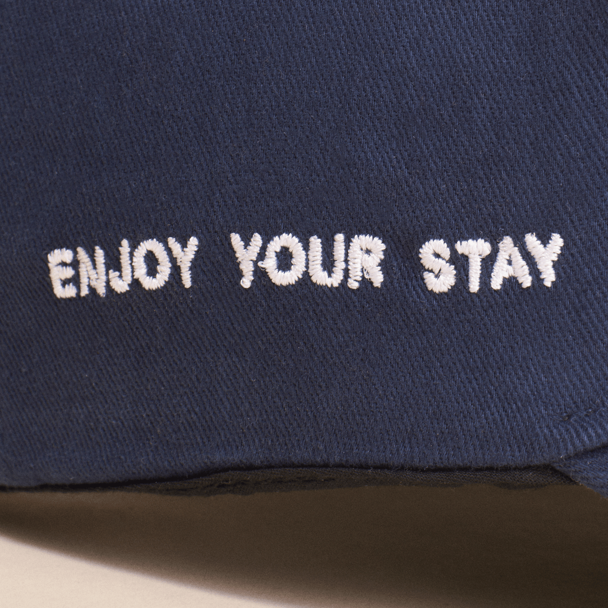 Close-up of Retro Brunch Cap showing white embroidered ENJOY YOUR STAY slogan on navy cotton fabric