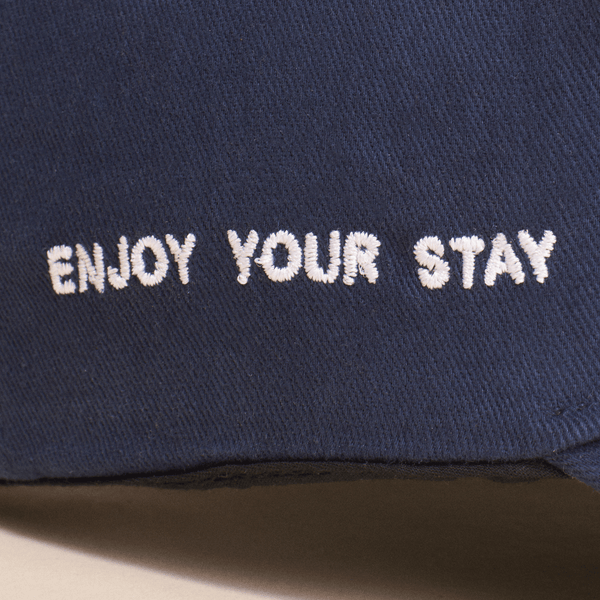 Close-up of Retro Brunch Cap showing white embroidered ENJOY YOUR STAY slogan on navy cotton fabric