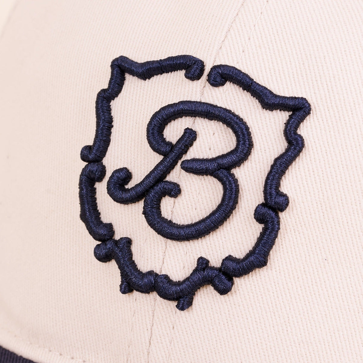 Close-up of Retro Crest cap front panel showcasing navy embroidered B crest on cream cotton fabric