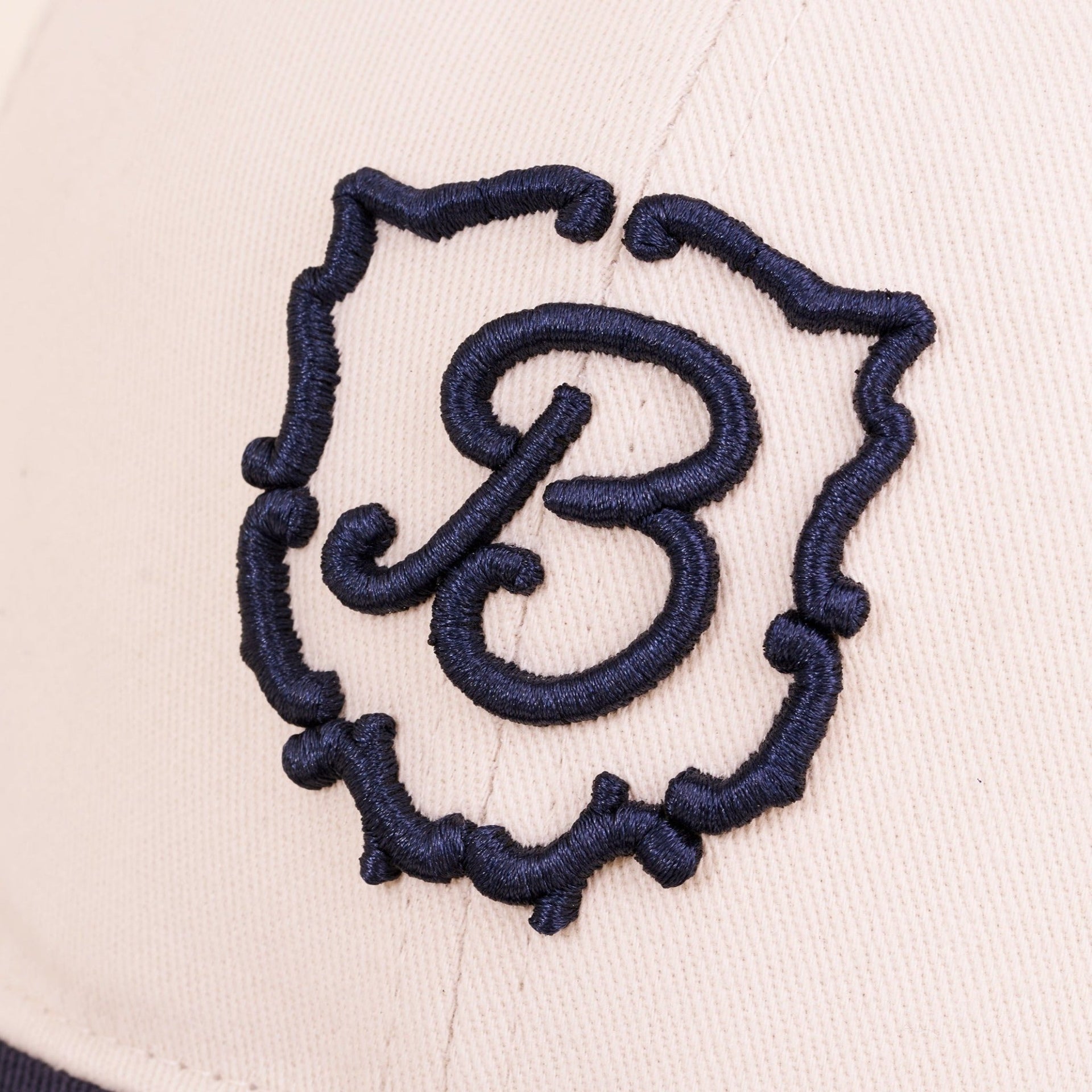 Close-up of Retro Crest cap front panel showcasing navy embroidered B crest on cream cotton fabric