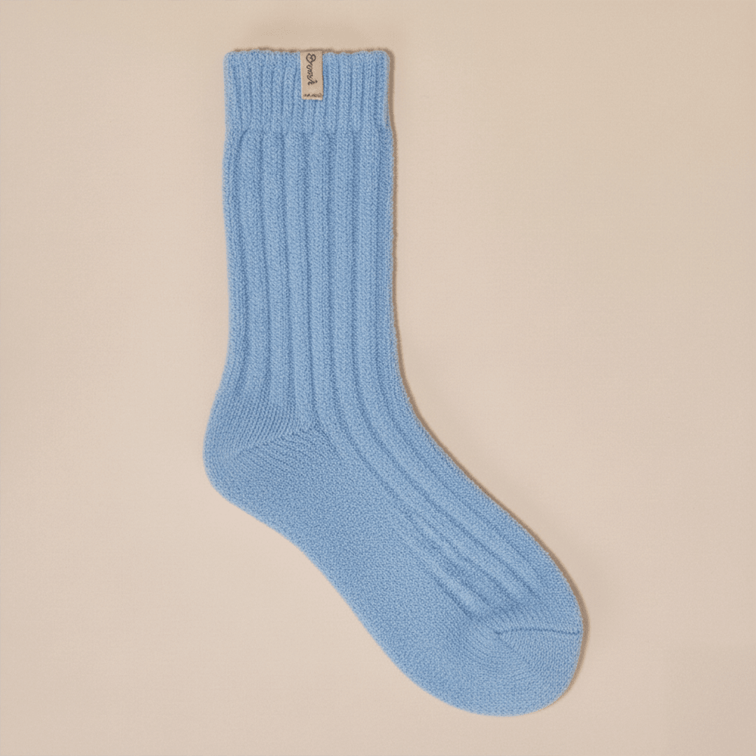 Flat lay of powder blue cashmere-wool crew sock showcasing ribbed knit texture and Brunch tab on beige background
