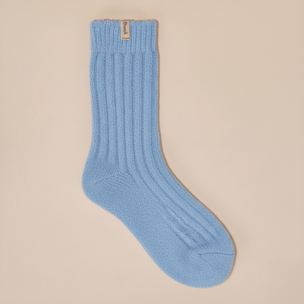 Flat lay of powder blue cashmere-wool crew sock showcasing ribbed knit texture and Brunch tab on beige background