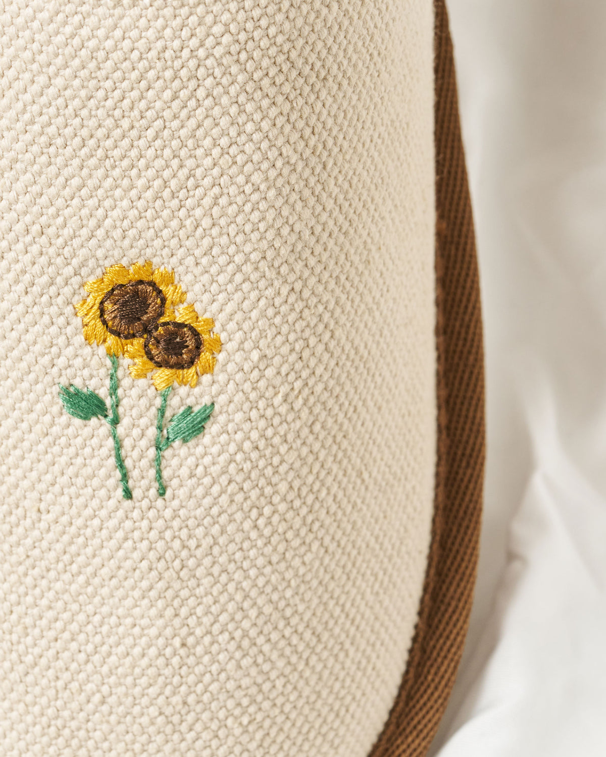 Close-up of Essential Floral canvas slipper in beige showing embroidered sunflower motif and textured woven upper with brown trim