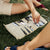 Person moving a checker on an open beige suede travel backgammon set laid on grass