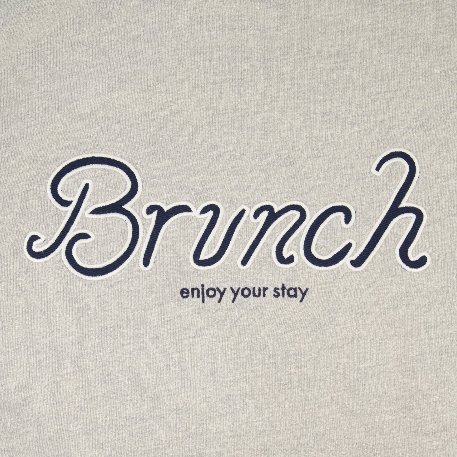 Close-up of Varsity Crewneck showing embroidered navy Brunch script and small enjoy your stay text on heather grey French terry
