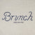Close-up of Varsity Crewneck showing embroidered navy Brunch script and small enjoy your stay text on heather grey French terry