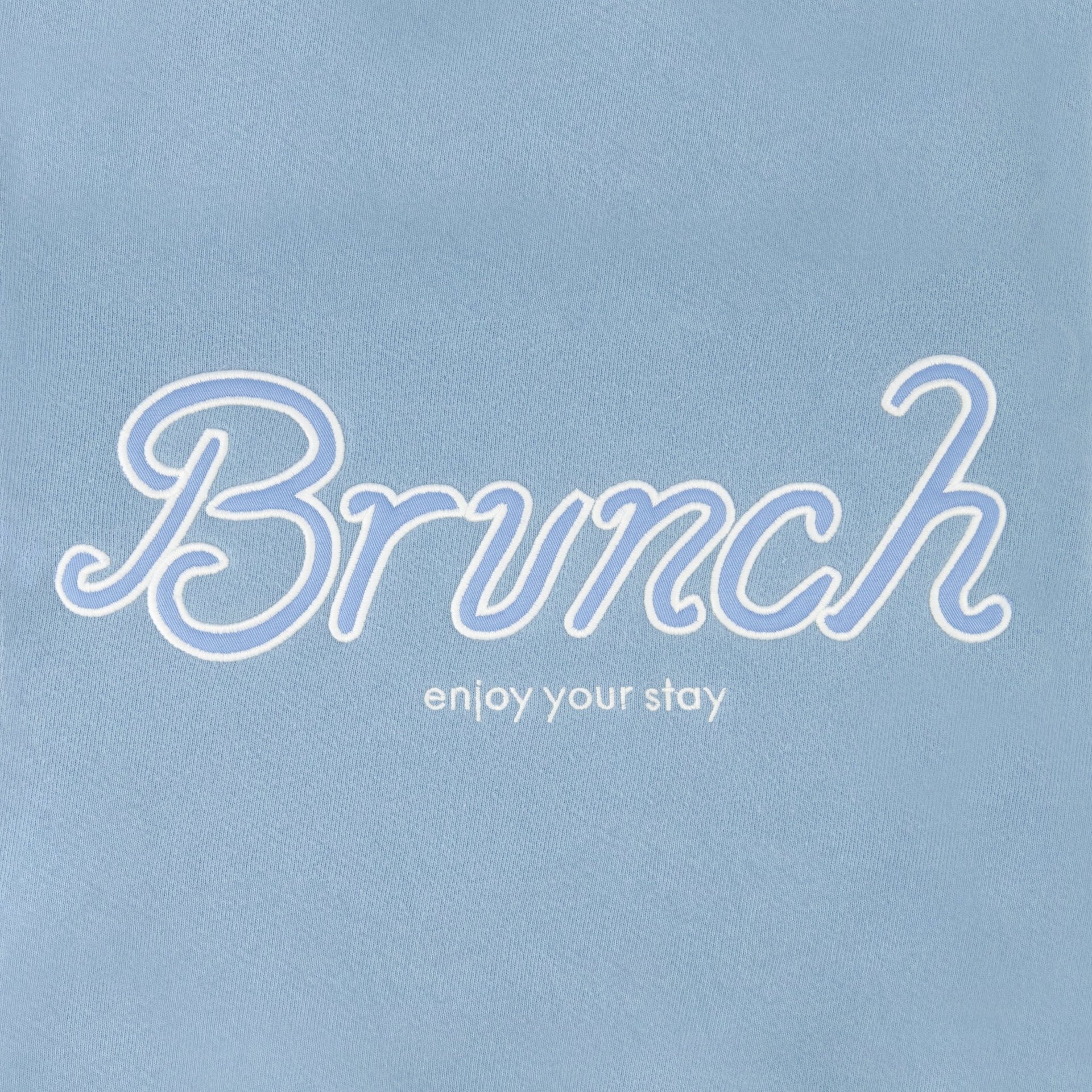Close-up front of Varsity Crewneck showing embroidered Brunch script and enjoy your stay tagline on powder blue French terry
